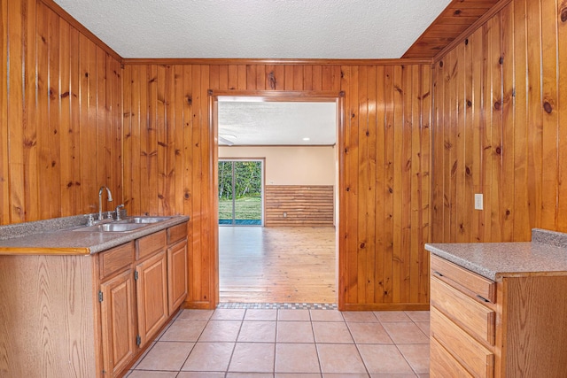 kitchen featuring light tile patterned floors, a sink, light countertops, wood walls, and a textured ceiling