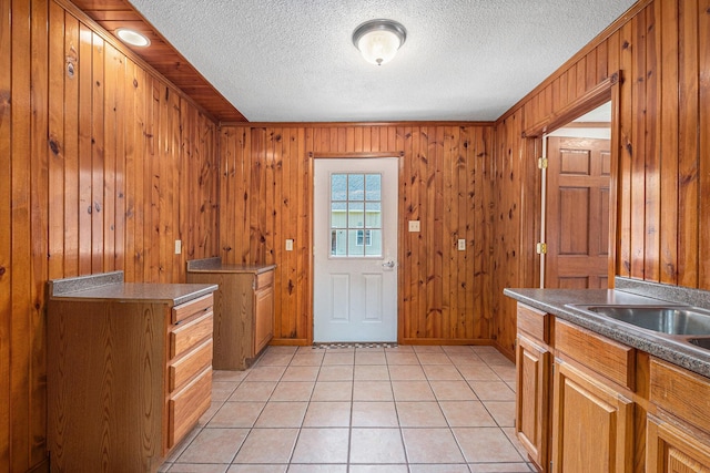 doorway with light tile patterned floors, a textured ceiling, and baseboards