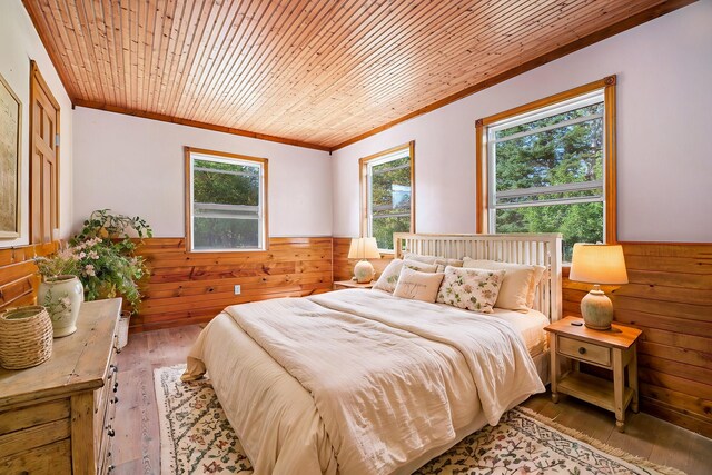 bedroom with light wood-type flooring, a wainscoted wall, ornamental molding, wooden walls, and wooden ceiling