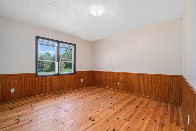 empty room with a wainscoted wall, light wood-style flooring, and a textured ceiling