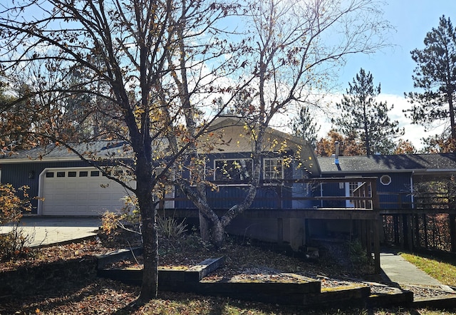 rear view of property with a garage, concrete driveway, a deck, and a carport