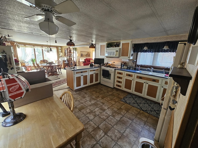 kitchen featuring white appliances, a peninsula, a sink, a textured ceiling, and dark countertops