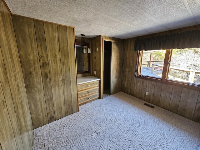 bedroom with a textured ceiling, visible vents, wooden walls, and light carpet