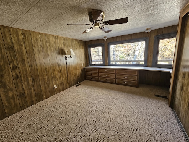 unfurnished bedroom featuring a textured ceiling, visible vents, wooden walls, built in desk, and light carpet