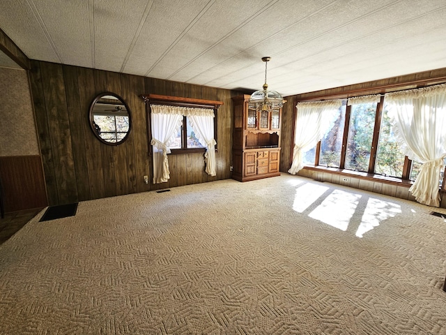 unfurnished dining area with a textured ceiling, carpet floors, wooden walls, visible vents, and a notable chandelier