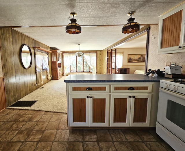 kitchen featuring visible vents, wooden walls, a peninsula, dark countertops, and white gas range oven