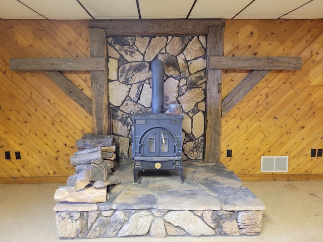 details featuring wooden walls, visible vents, a wood stove, and a paneled ceiling