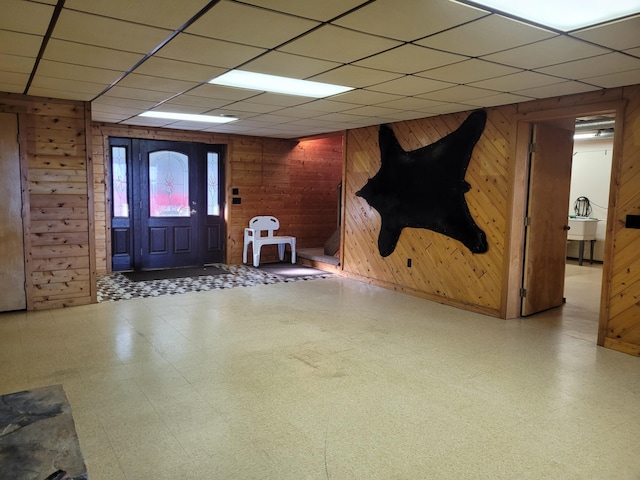 entrance foyer with tile patterned floors, a paneled ceiling, and wood walls