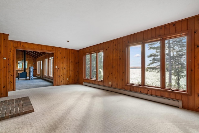 unfurnished living room featuring a healthy amount of sunlight, a baseboard heating unit, carpet, and a wood stove