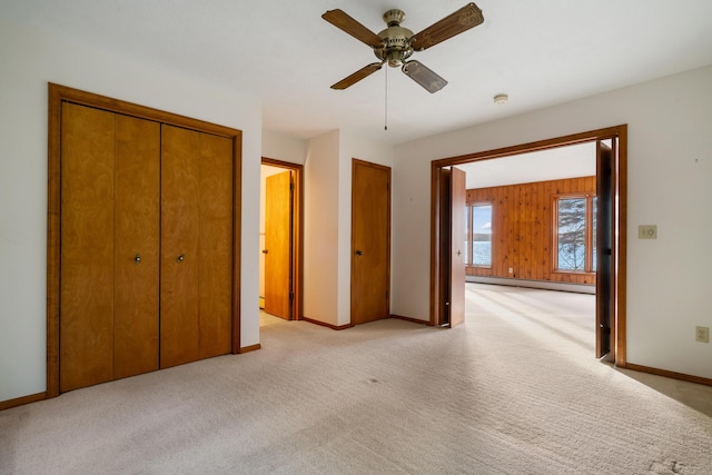 unfurnished bedroom with wooden walls, a baseboard heating unit, ceiling fan, baseboards, and light carpet