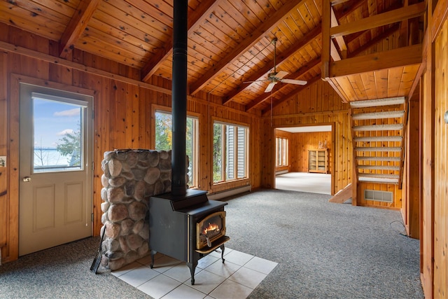 unfurnished living room featuring a wood stove, plenty of natural light, wood walls, and carpet floors