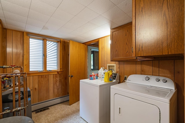 clothes washing area with washing machine and dryer, light floors, wood walls, baseboard heating, and cabinet space