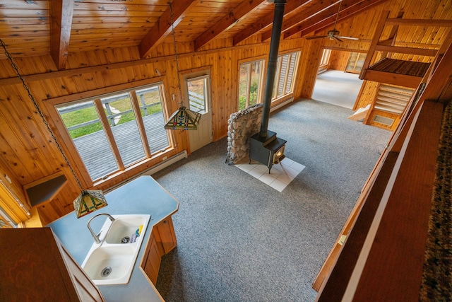 living room with wooden walls, lofted ceiling with beams, a wood stove, and carpet