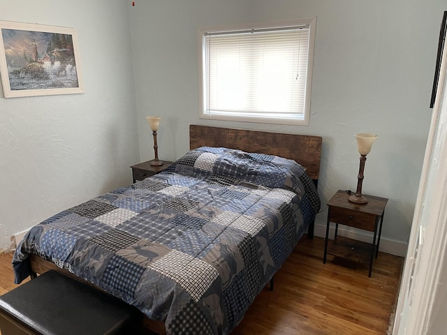 bedroom featuring a textured wall, baseboards, and wood finished floors