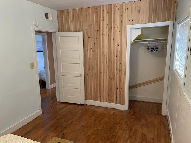 unfurnished bedroom with visible vents, baseboards, wood walls, a closet, and wood-type flooring