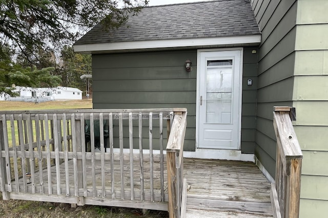 entrance to property featuring a deck and a shingled roof