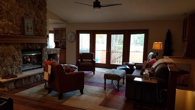 living room featuring a stone fireplace, vaulted ceiling, wood finished floors, and a ceiling fan