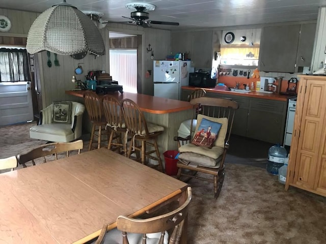 kitchen featuring white appliances, carpet, wood walls, and a ceiling fan