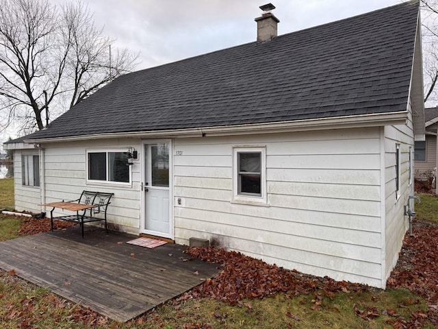 back of property with roof with shingles, a deck, and a chimney