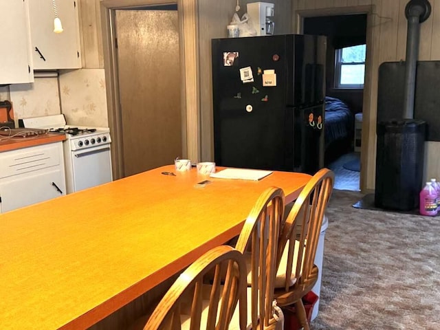 kitchen with white range with gas cooktop, a wood stove, freestanding refrigerator, white cabinetry, and carpet flooring