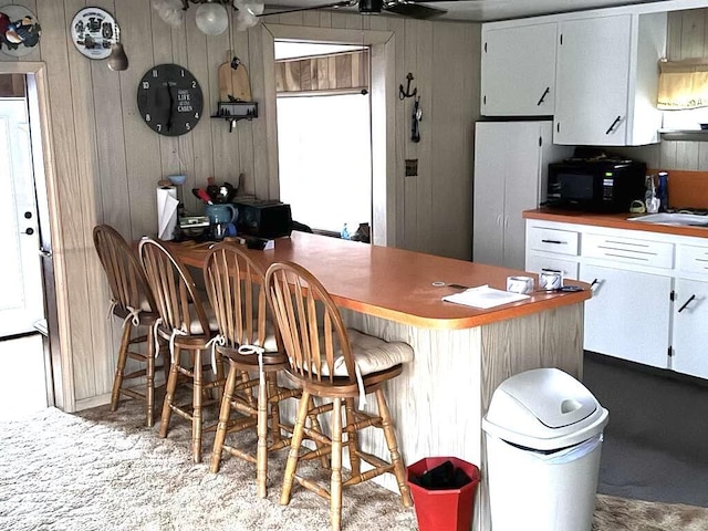 kitchen with wooden walls, white cabinets, freestanding refrigerator, and black microwave