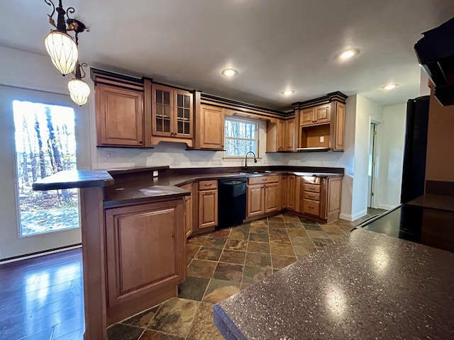 kitchen with a sink, black dishwasher, dark countertops, stone tile floors, and glass insert cabinets