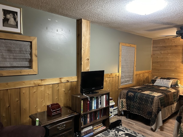 bedroom featuring wooden walls, wood finished floors, a wainscoted wall, and a textured ceiling