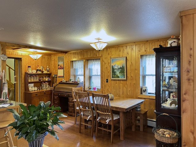 dining room featuring wooden walls, wood finished floors, baseboard heating, and a textured ceiling