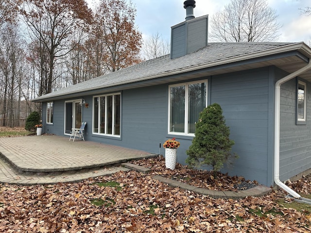 back of property featuring a shingled roof, a patio area, and a chimney