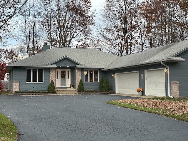 single story home with aphalt driveway, an attached garage, a shingled roof, brick siding, and a chimney