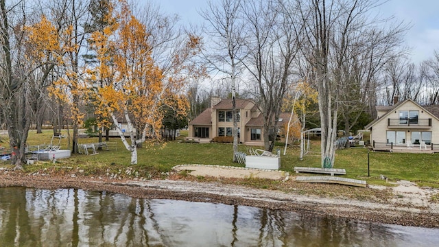 back of property with a yard, a water view, a vegetable garden, and a chimney