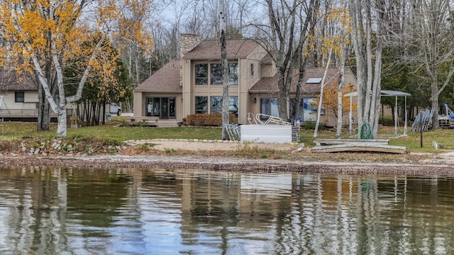 back of property with a water view, roof with shingles, and a chimney