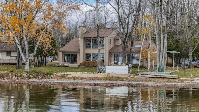 back of property with a chimney, roof with shingles, and a water view