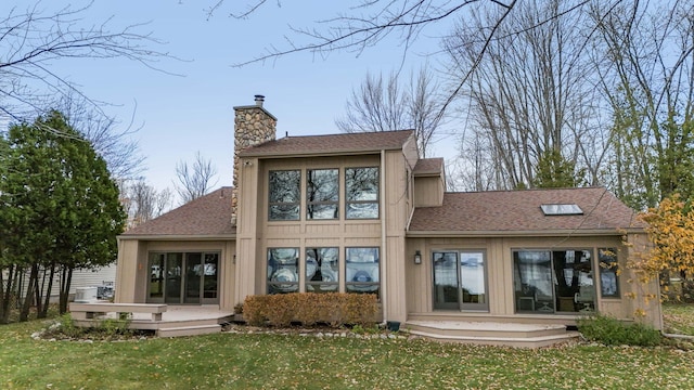 rear view of property with a lawn, roof with shingles, a deck, and a chimney