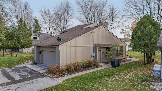 view of home's exterior with roof with shingles, driveway, a chimney, a garage, and a lawn