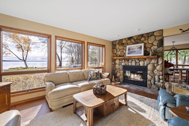 living area featuring a stone fireplace, wood finished floors, a water view, and baseboards