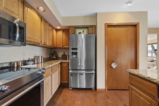 kitchen featuring light stone counters, brown cabinetry, recessed lighting, light wood-style floors, and appliances with stainless steel finishes