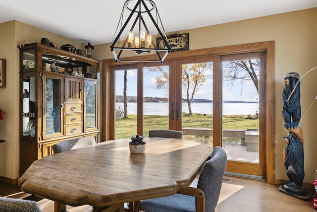 dining room featuring a wealth of natural light, light wood-type flooring, a water view, and a notable chandelier