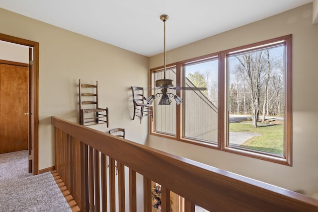 hallway with an upstairs landing, baseboards, and carpet