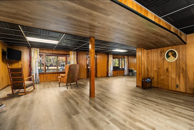 basement featuring baseboards, plenty of natural light, wooden walls, and wood finished floors