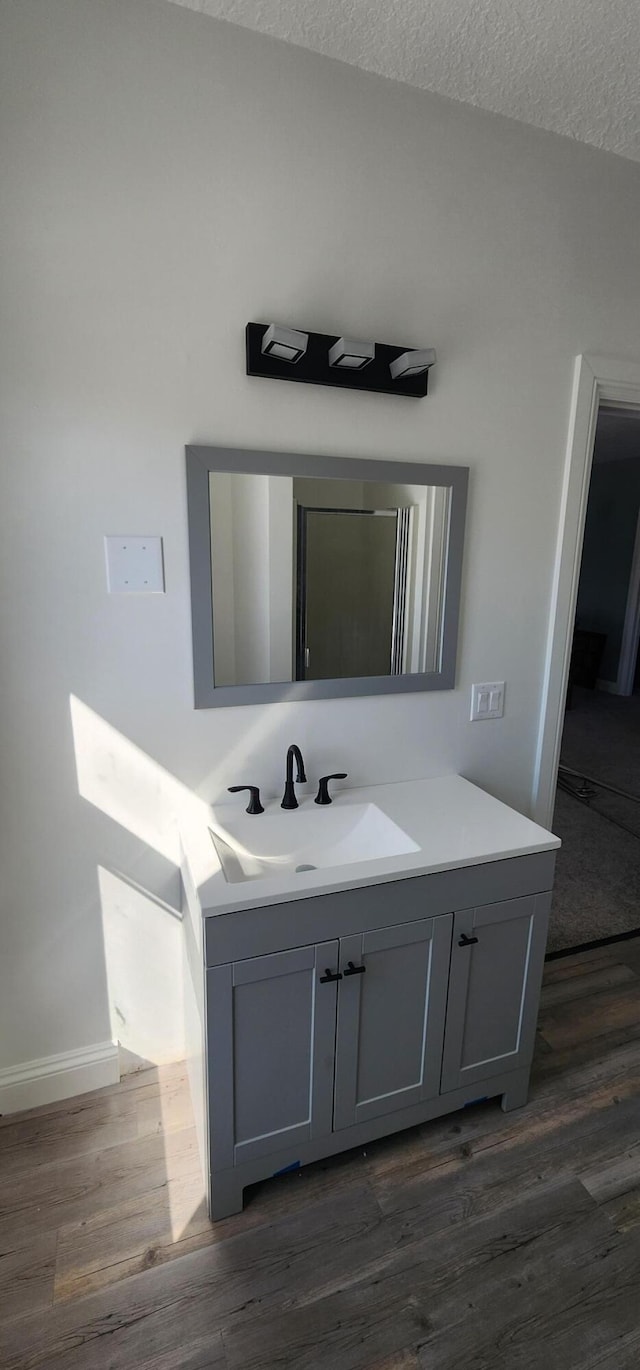 bathroom featuring a textured ceiling, vanity, baseboards, and wood finished floors