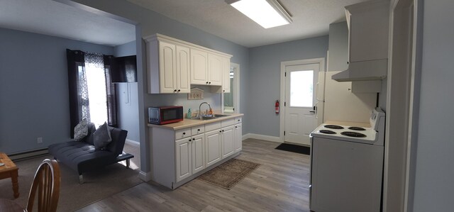 kitchen featuring under cabinet range hood, a baseboard heating unit, a sink, white electric stove, and a healthy amount of sunlight