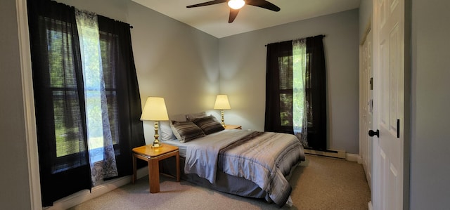 bedroom with a baseboard heating unit, multiple windows, baseboards, and light carpet