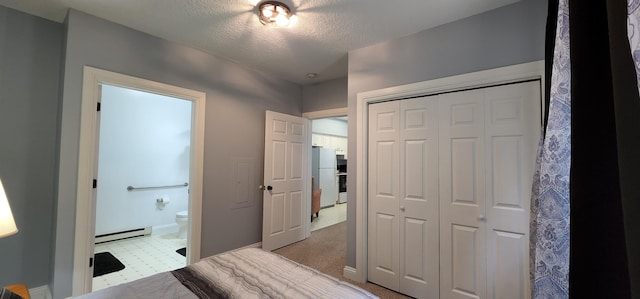 bedroom featuring ensuite bathroom, a textured ceiling, freestanding refrigerator, a closet, and baseboard heating