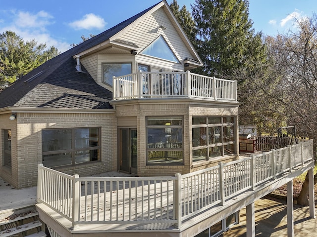 rear view of property featuring brick siding, a deck, and a balcony