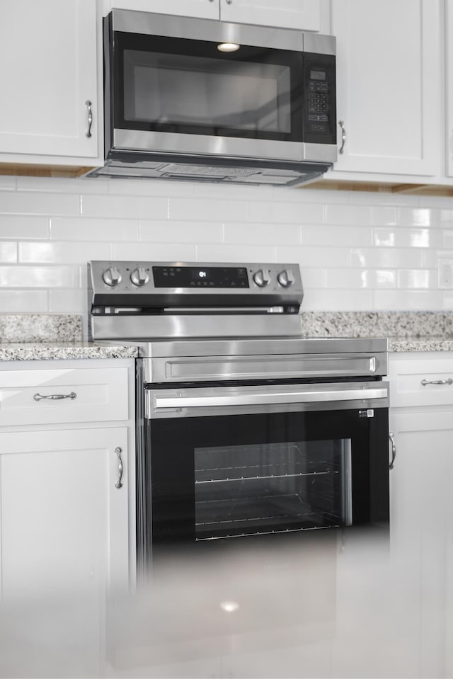 kitchen with backsplash, appliances with stainless steel finishes, white cabinetry, and light stone countertops