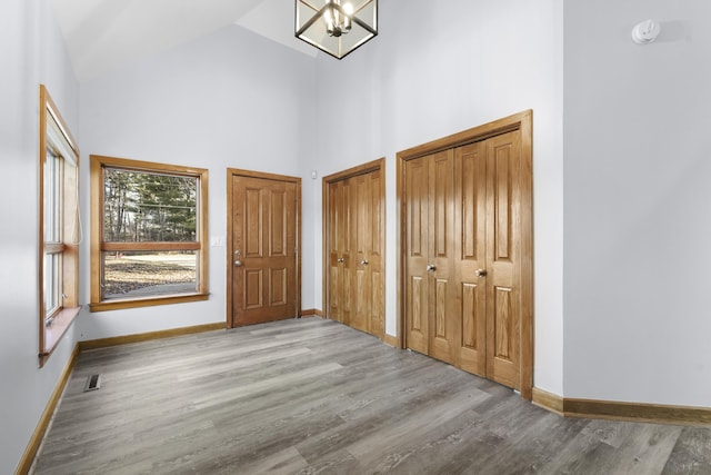 entryway featuring baseboards, high vaulted ceiling, an inviting chandelier, and wood finished floors