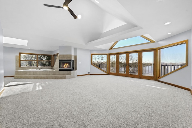 unfurnished living room with carpet floors, plenty of natural light, lofted ceiling with skylight, and a tiled fireplace