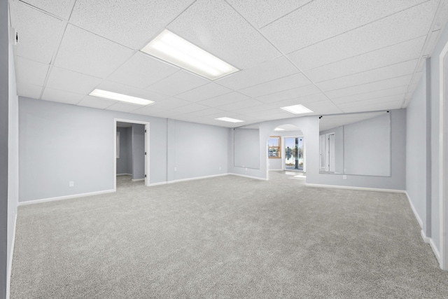 basement with arched walkways, a drop ceiling, baseboards, and carpet