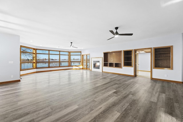 unfurnished living room featuring a wealth of natural light, baseboards, wood finished floors, and a glass covered fireplace